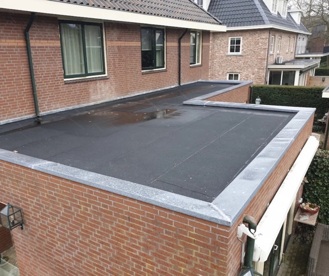 Zwart bitumen plat dak op een aanbouw met nieuwe daktrim en zinken afvoer