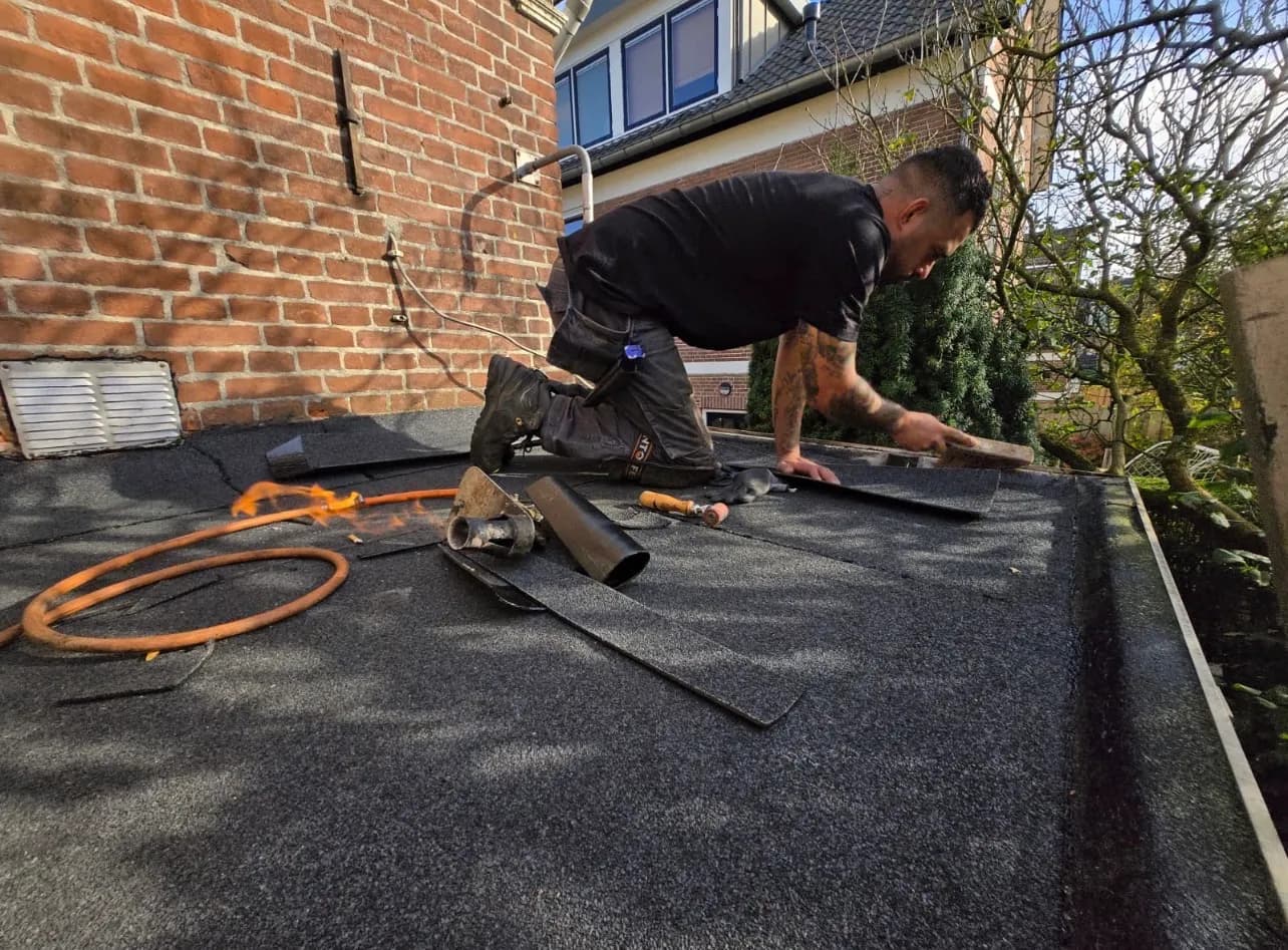 Raymond Hoonhorst snijdt bitumen op maat op een plat dak