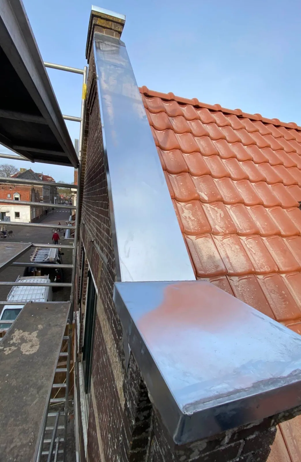 Schoorsteen op een pannendak, nieuw bekleed in zink, met steiger langs de gevel