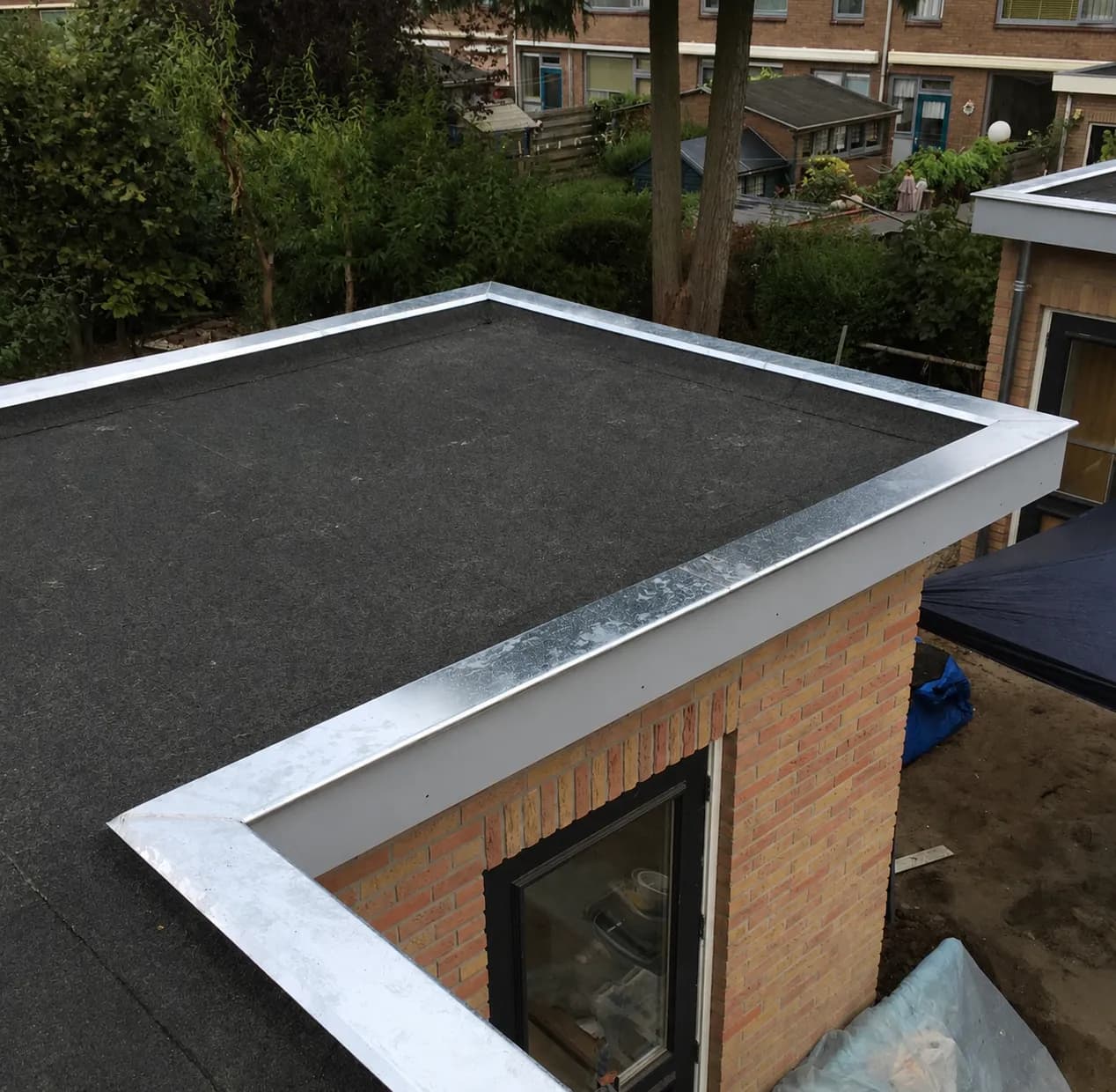 Zwart bitumen dak op een bakstenen aanbouw met nieuwe zinken daktrim rondom, gezien van bovenaf