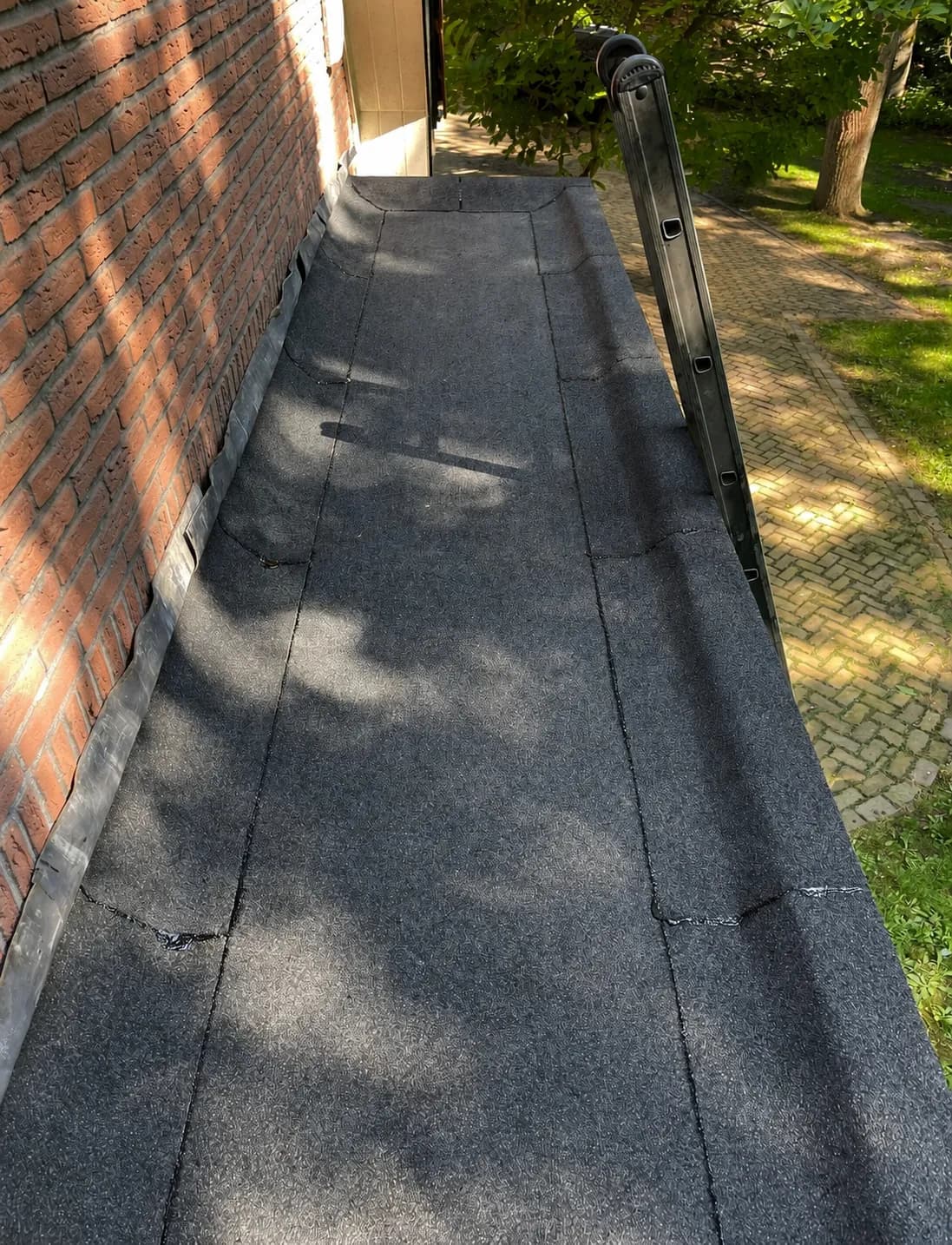 Smal bitumen dak langs een bakstenen gevel met loodslabben, ladder tegen de dakrand